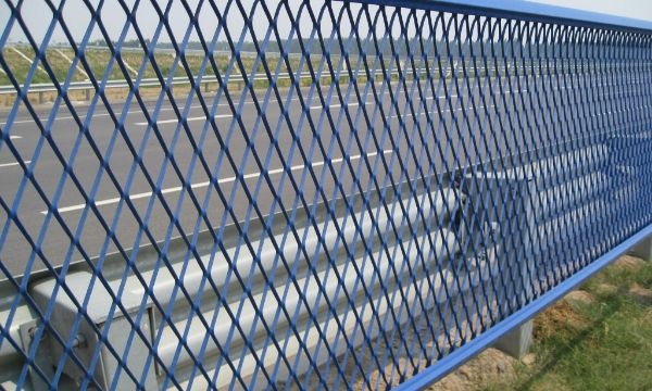 Blue anti-glare expanded metal security fence is installed along the road.