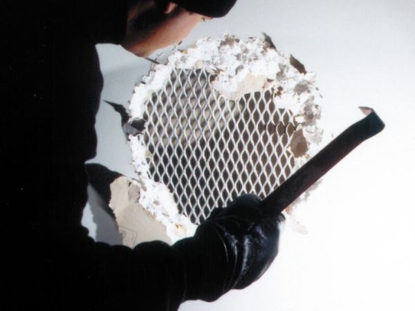 A man in black cut a hole on the wall and show the expanded metal inside the wall.