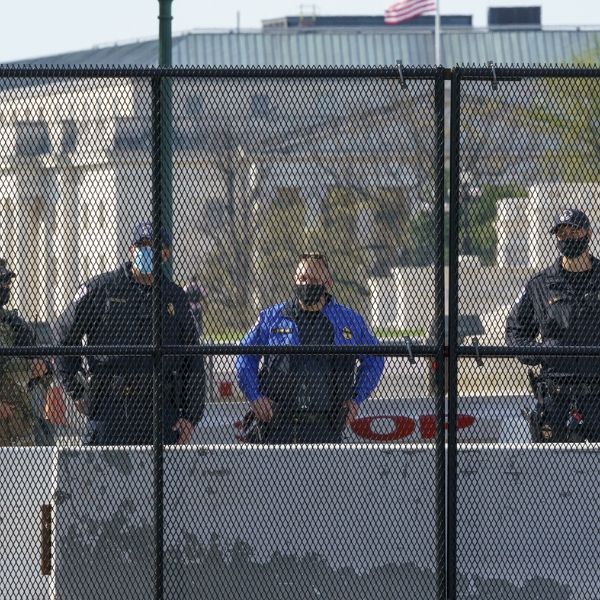 Several men are standing outside the government agency expanded metal security fence.